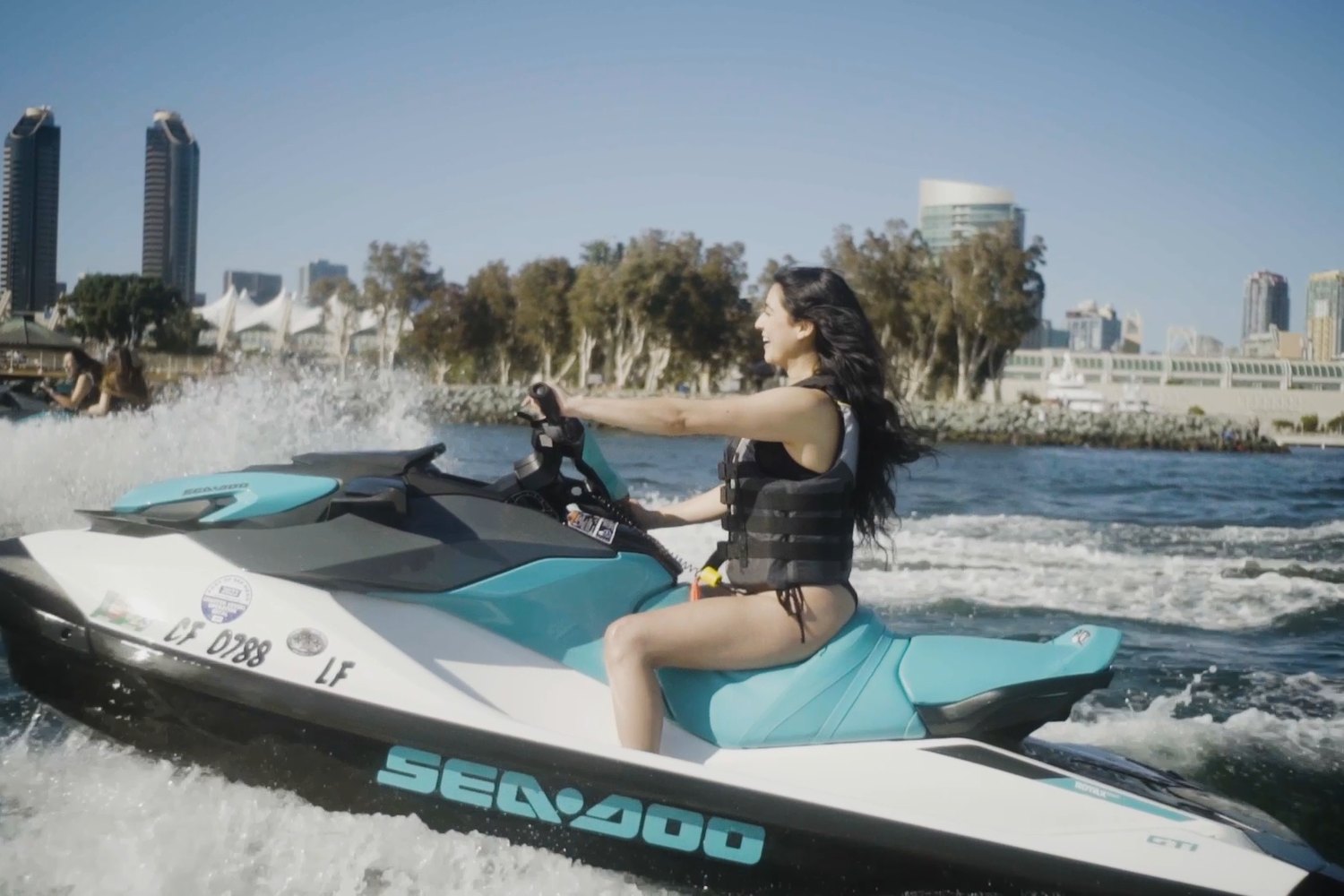 Woman riding a teal and white jet ski through the spray